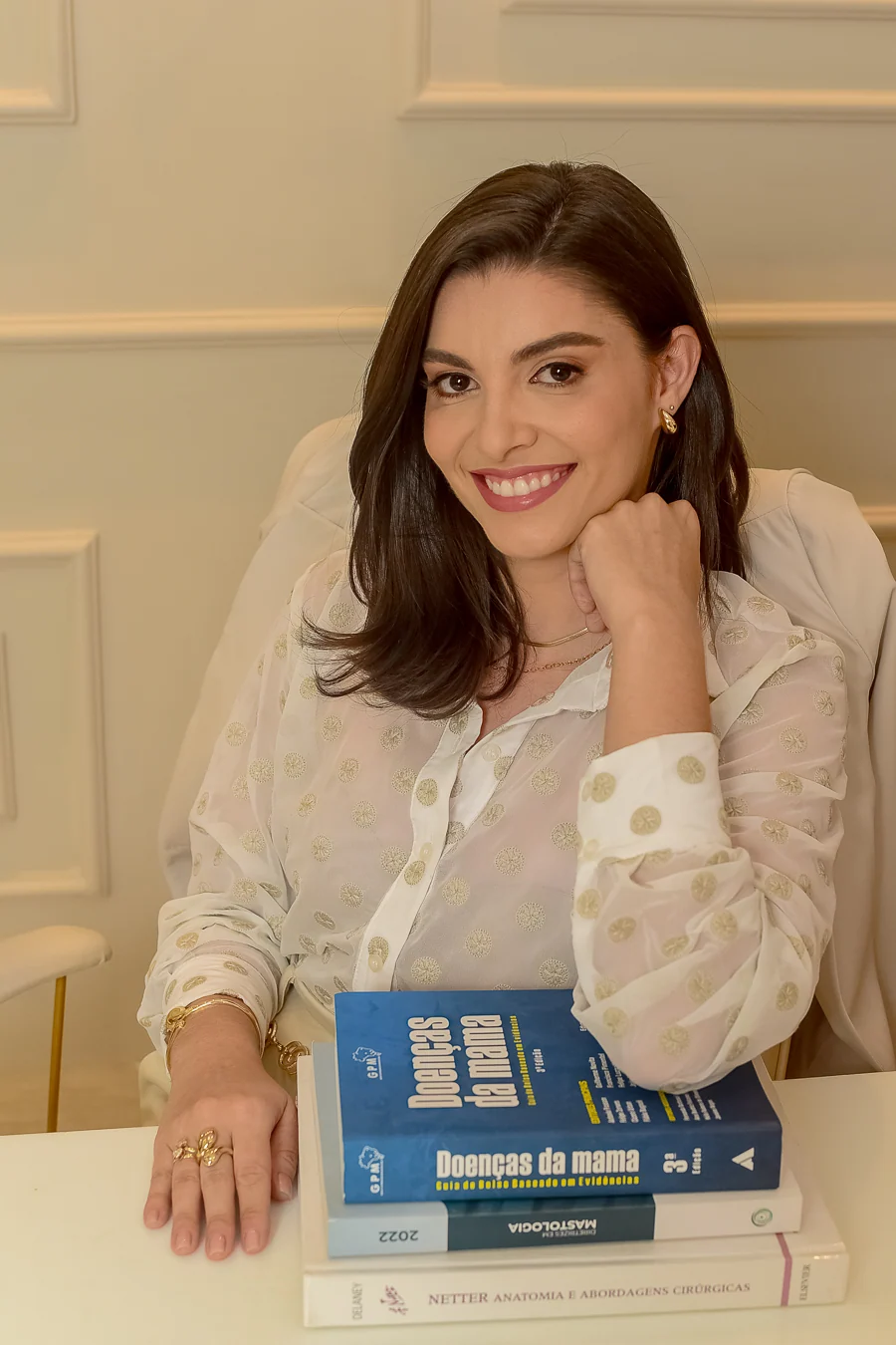 Dra. Fernanda Borba com blusa branca no consultório, apoiada sobre livros